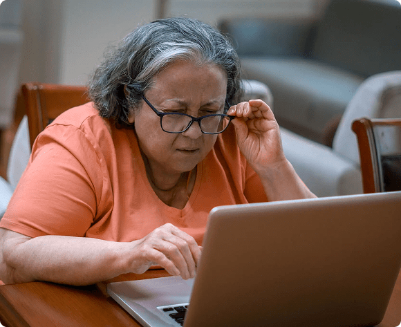 Elderly woman intently using a laptop at home.